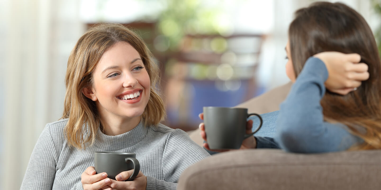 Lächelnde Frauen tauschen bei einer Tasse Tee ihre Erfahrungen mit Lyranda gegen Lippenherpes aus