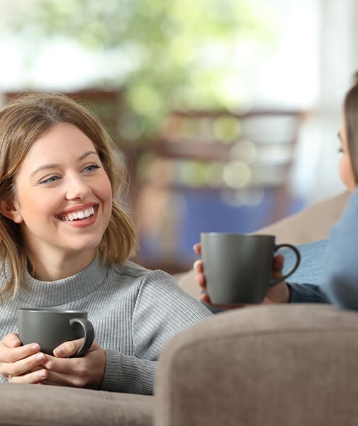 Lächelnde Frauen tauschen bei einer Tasse Tee ihre Erfahrungen mit Lyranda gegen Lippenherpes aus