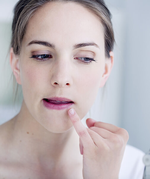 Frau untersucht ihre Lippen im Spiegel, da sie Symptome eines Herpes verspürt
