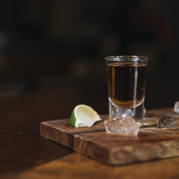 Ein Glass Alkohol steht auf einem Holzbrett mit einer Limette und mehreren Eiswürfeln.