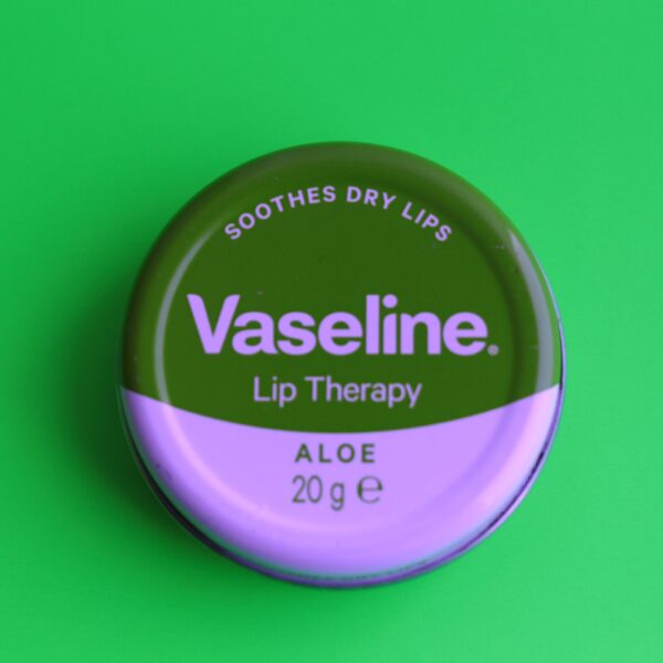 Eine Runde Dose mit der Aufschrift „Vaseline“ liegt auf einem grünen Hintergrund.
